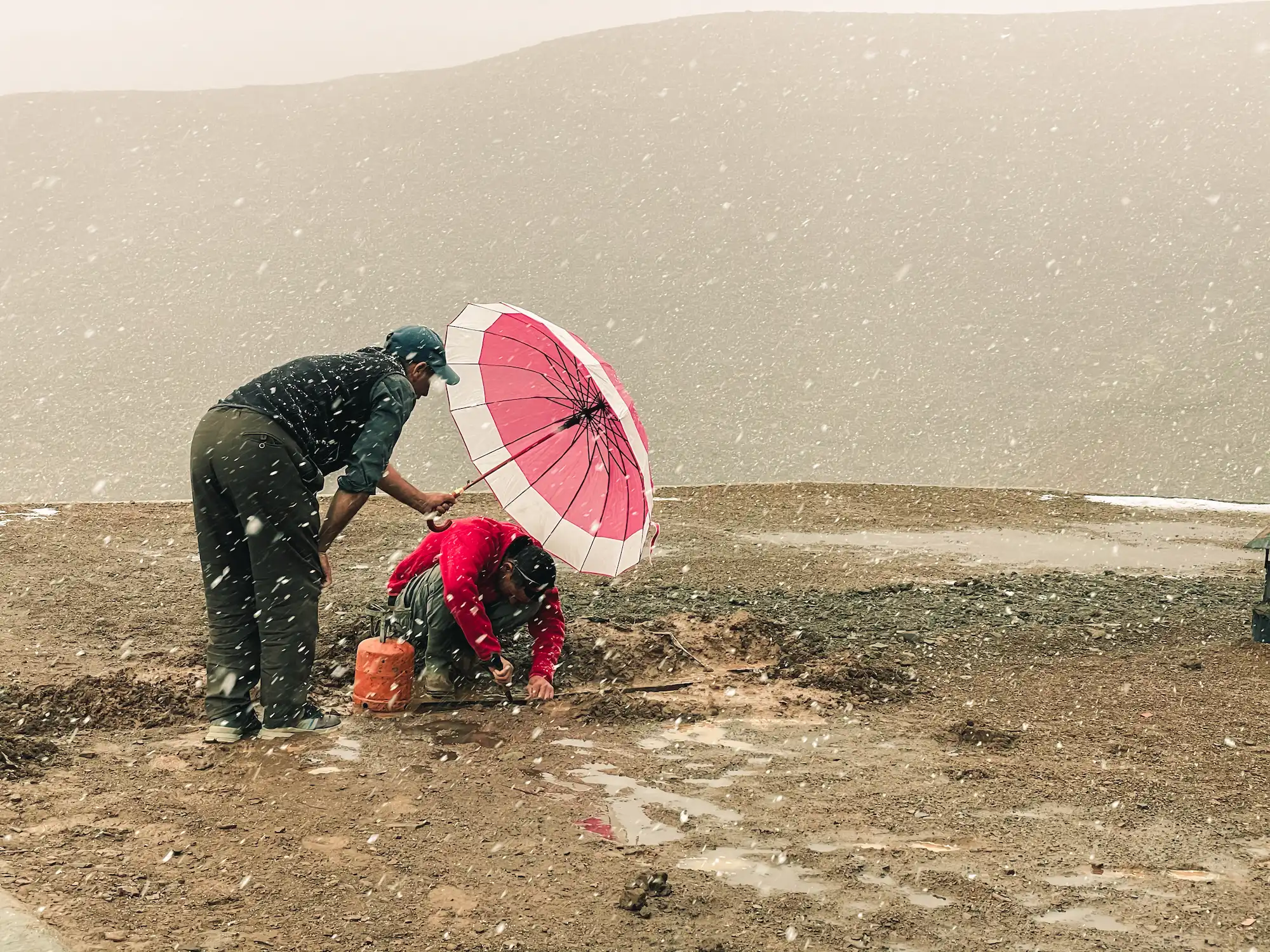 Deux personnes travaillant sur le toit do touda ecolodge sous la neige avec un parapluie rouge et blanc 