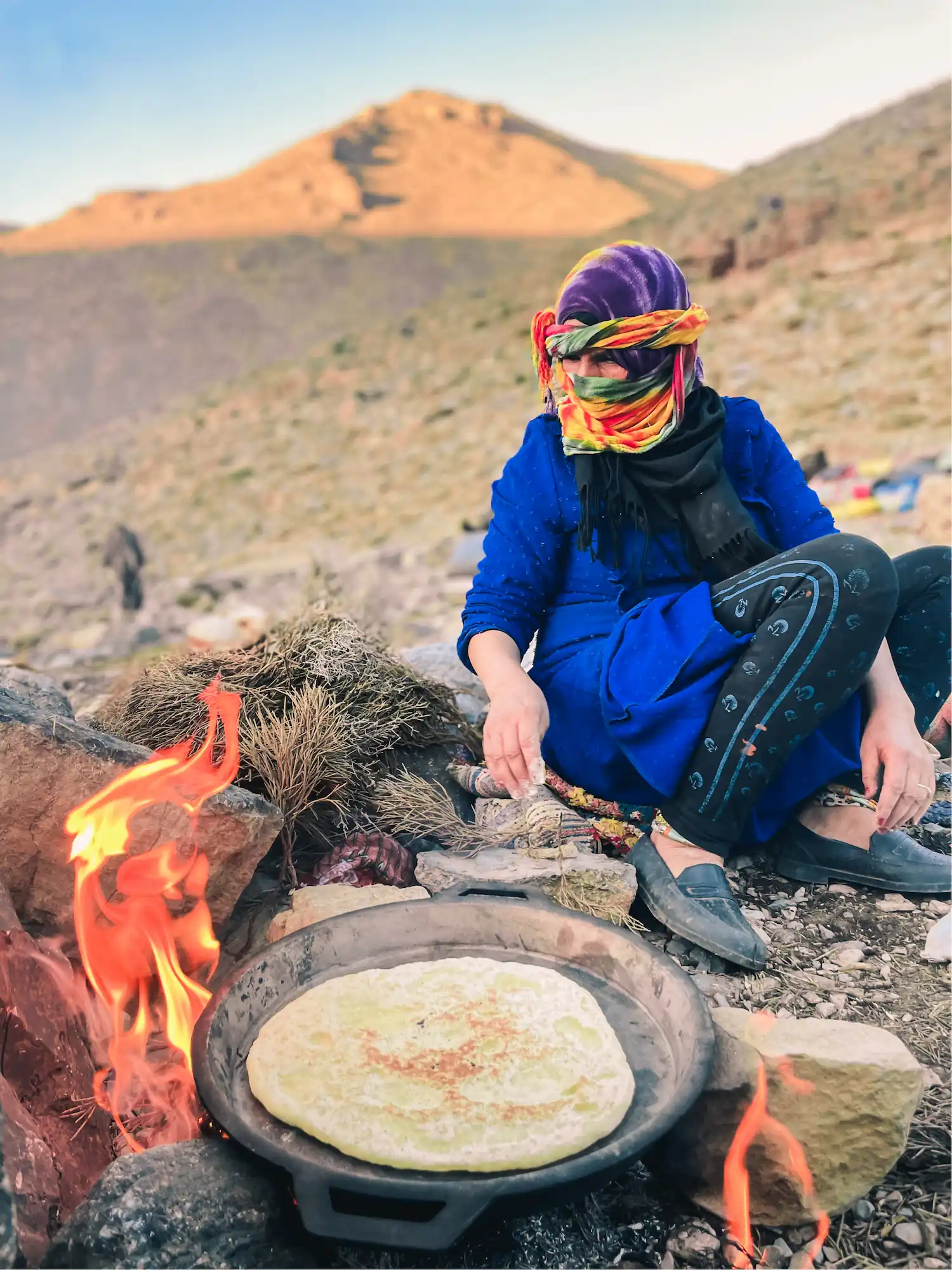 Femme nomade Aït Atta cuisant une galette de pain sur un feu de bois au campement, transhumance dans le Haut Atlas