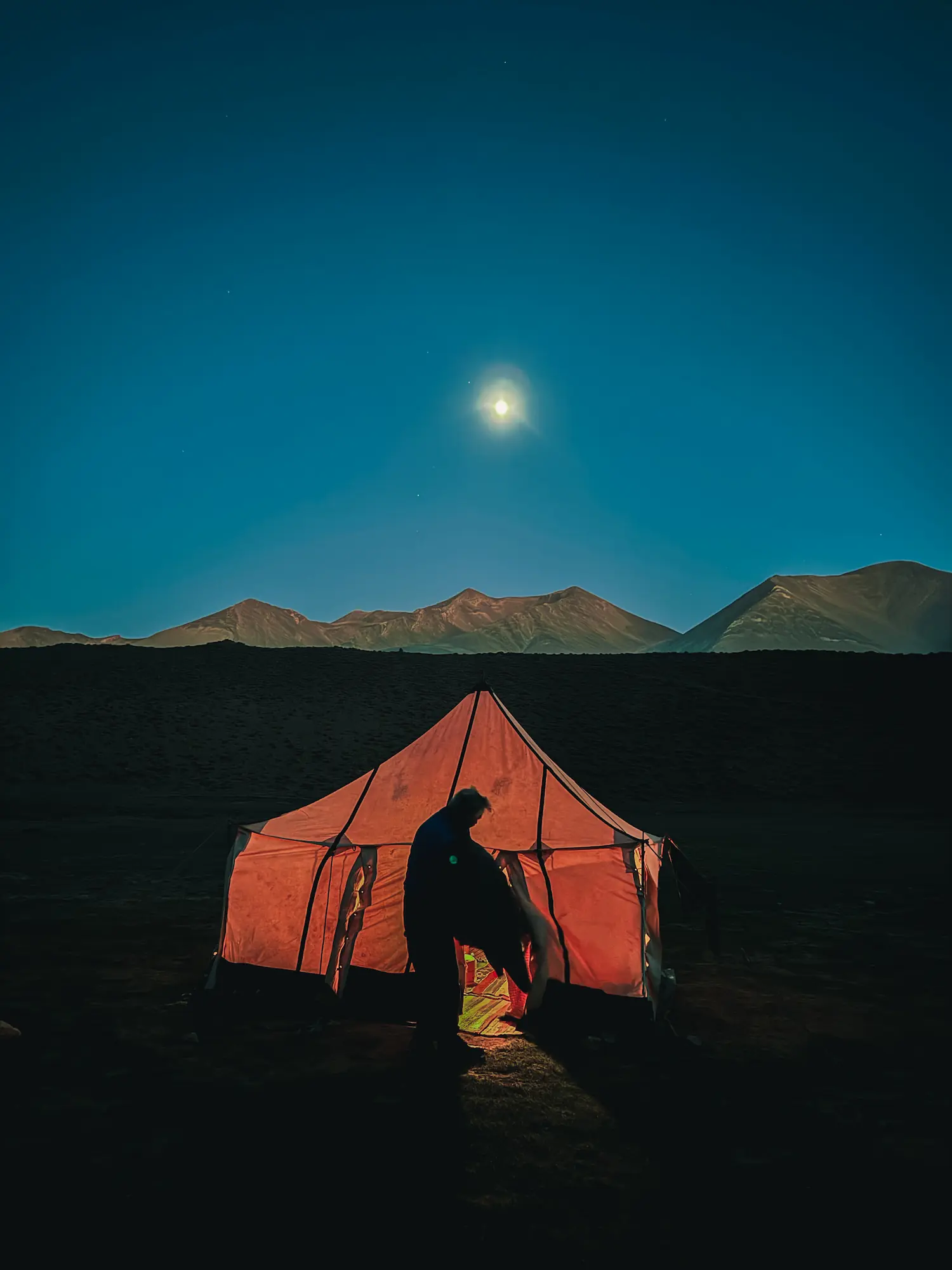 Glowing orange tent under a bright full moon at a high-altitude campsite near Touda Ecolodge.