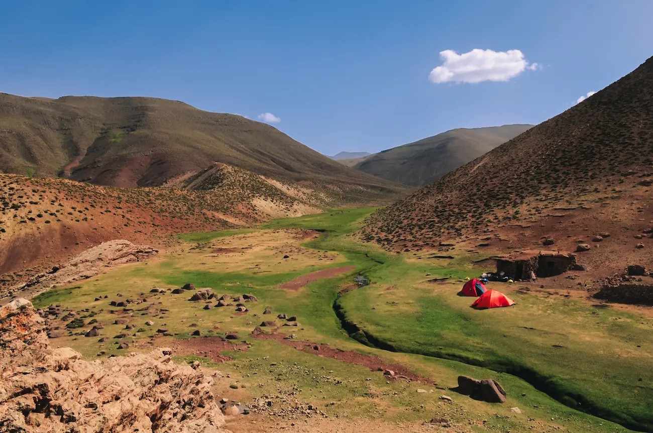 Red camping tents set up in a lush green mountain valley during a M'Goun trek with Touda Ecolodge.