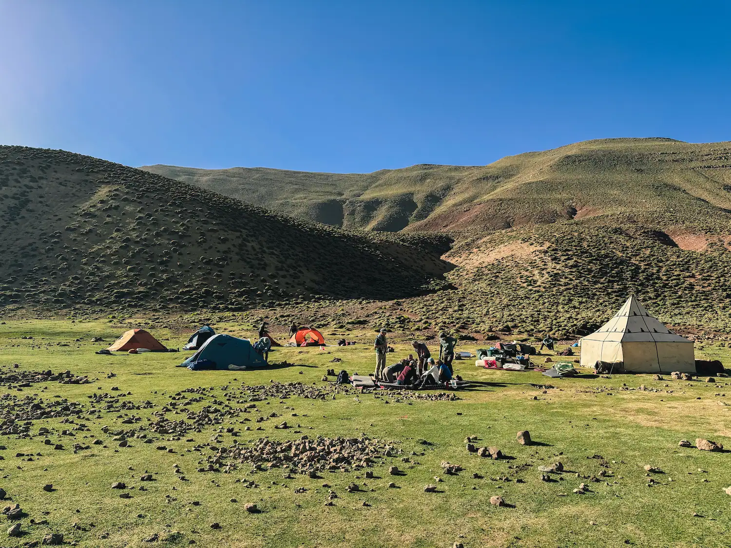 Trekking campsite with colourful tents and hikers gathered on a green meadow in the M'Goun valley with Touda Ecolodge.