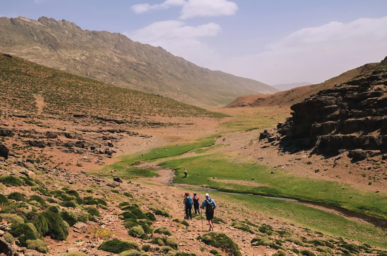 Trekkers walking along a small stream in a dry, rocky valley in the High Atlas with Touda Ecolodge.