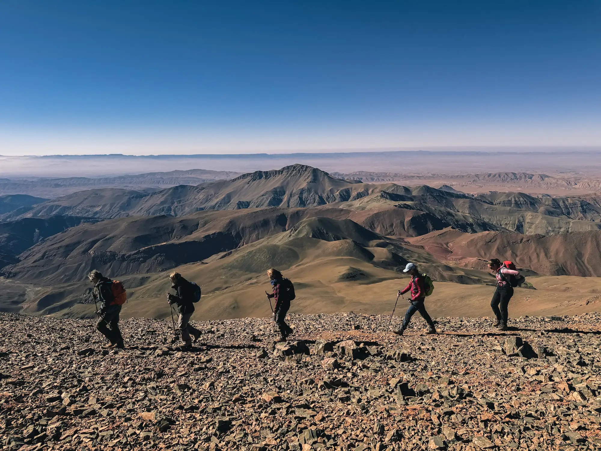 Groupe de randonneurs marchant en file indienne sur une haute crête rocheuse surplombant les montagnes avec Touda Ecolodge.