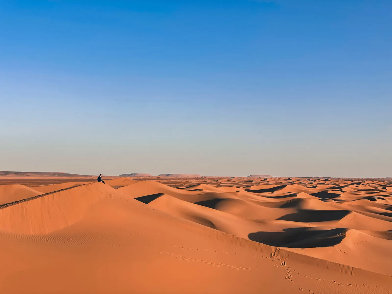 Personne assise seule au sommet d'une grande dune contemplant l'horizon avec Touda Ecolodge.