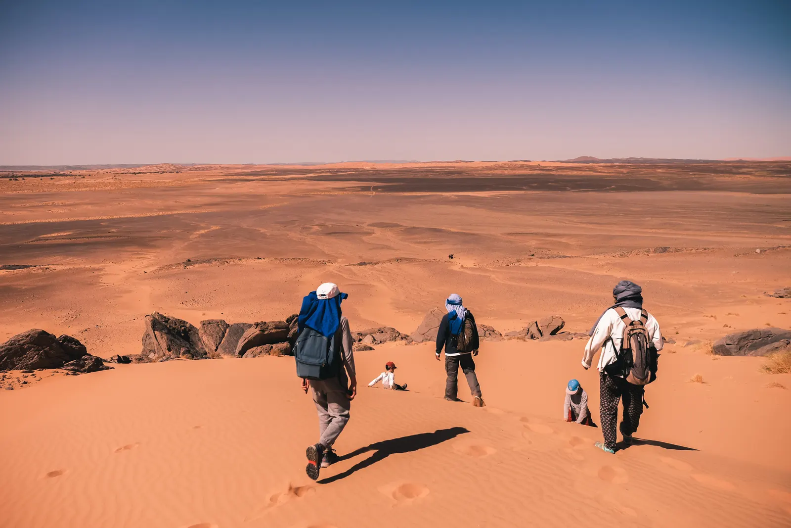 Group of a family hikers walking down a large sand dune in the moroccan sahara during a desert trek with Touda Ecolodge.