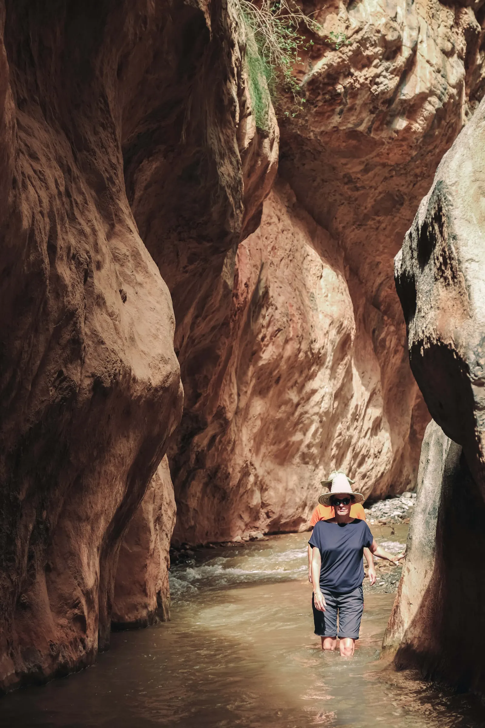 Wanderer gehen durch das Wasser zwischen den engen Felswänden der M'Goun-Schlucht mit Touda Ecolodge.