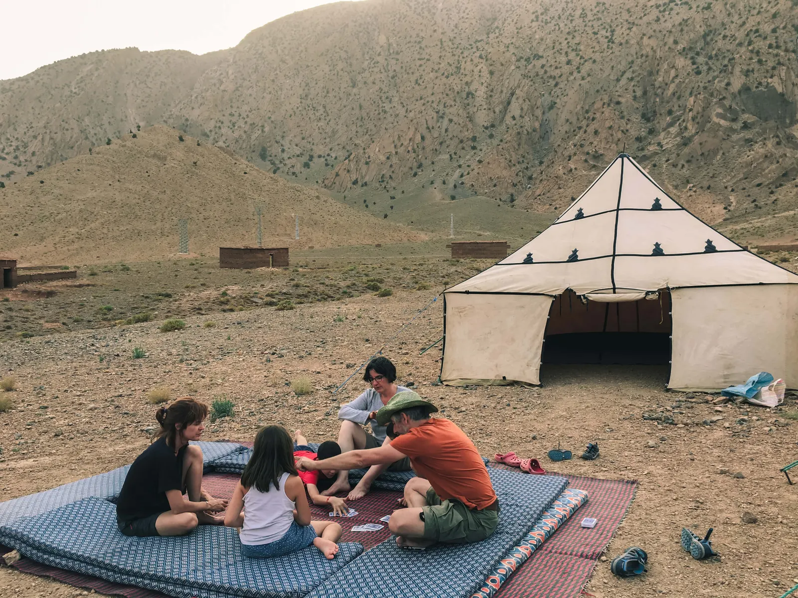 Family playing card games together on traditional mats outside their campsite tent with Touda Ecolodge.