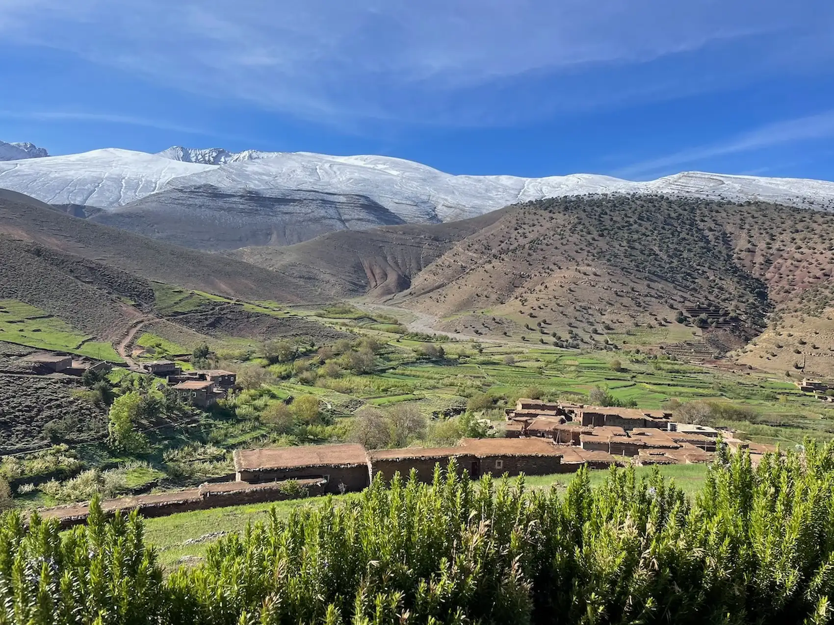 Berber earthen village and green fields below the snow-capped peaks, Aït Bouguemez Valley in spring