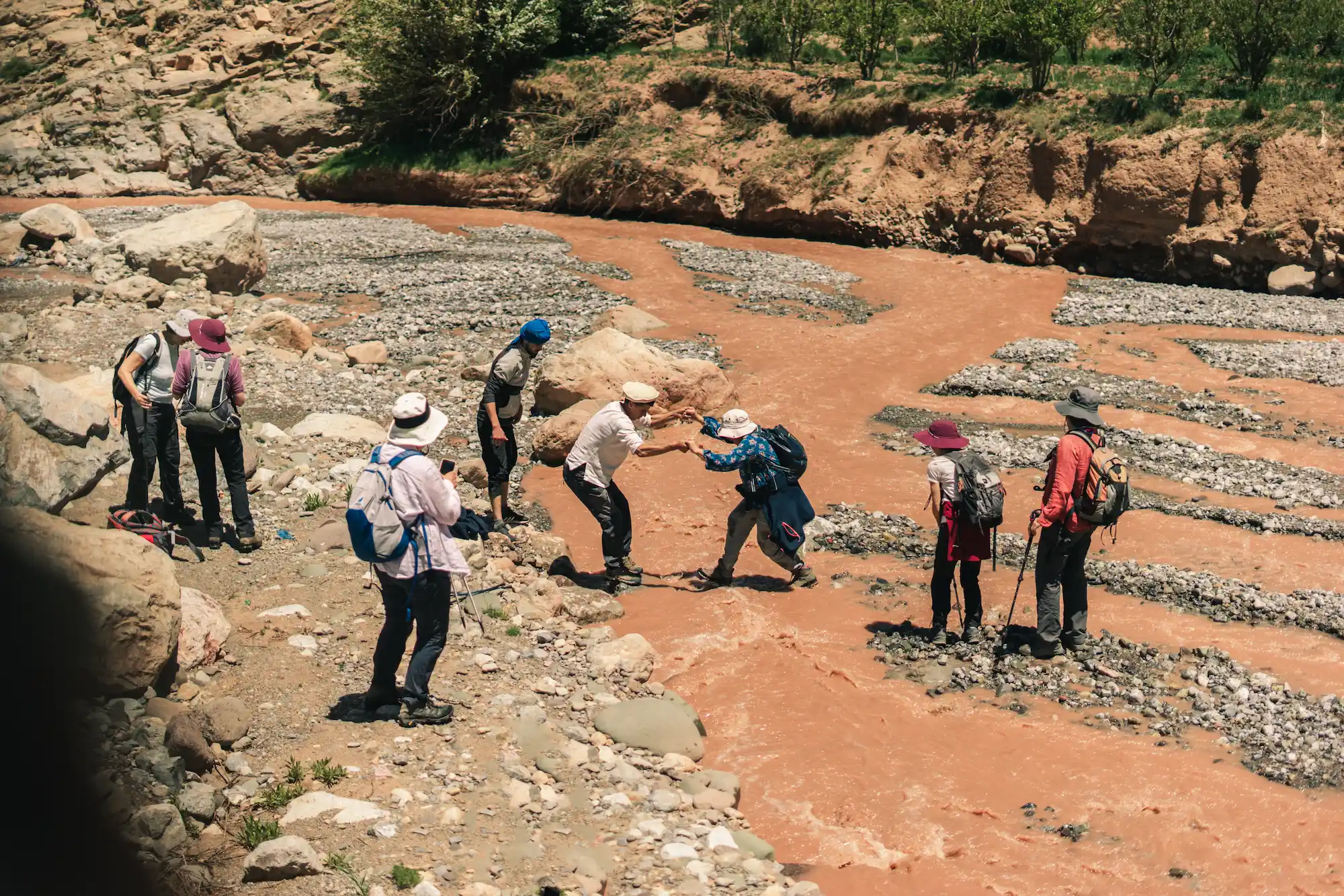 Hikers helping each other across a riverbed in the Aït Bougmez valley