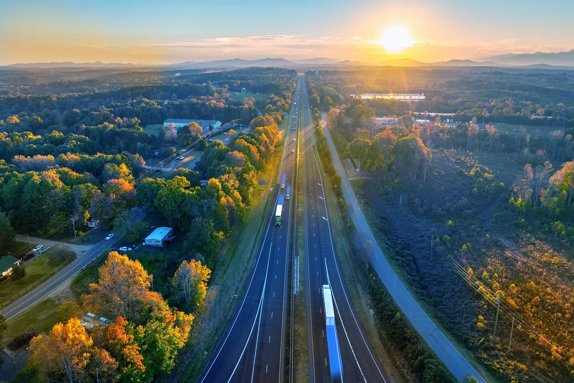 Aerial view of a highway at sunset surrounded by trees and open landscape