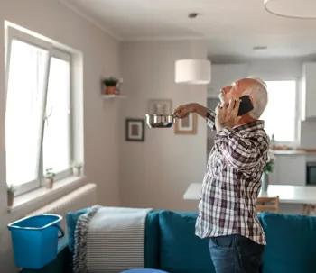 Homeowner using a bowl and phone during a ceiling leak emergency.