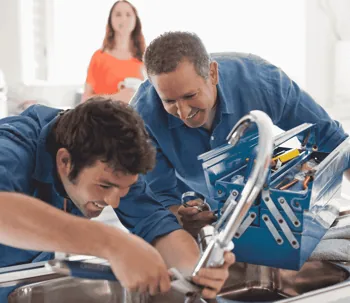 Professional plumbers in Huntington Beach fixing residential plumbing with a happy customer in the b…