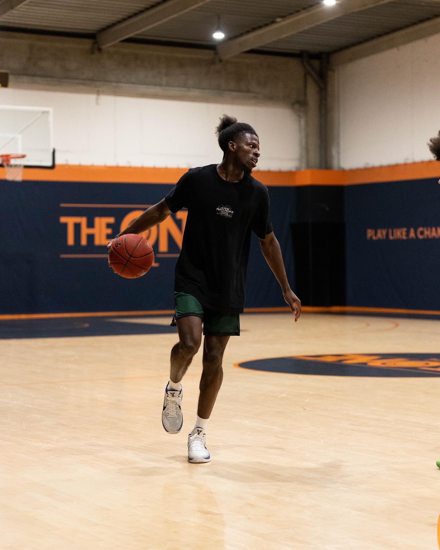 Jeune homme jouant au basketball en intérieur, dribblant le ballon sur un terrain avec des murs bleu foncé et orange.