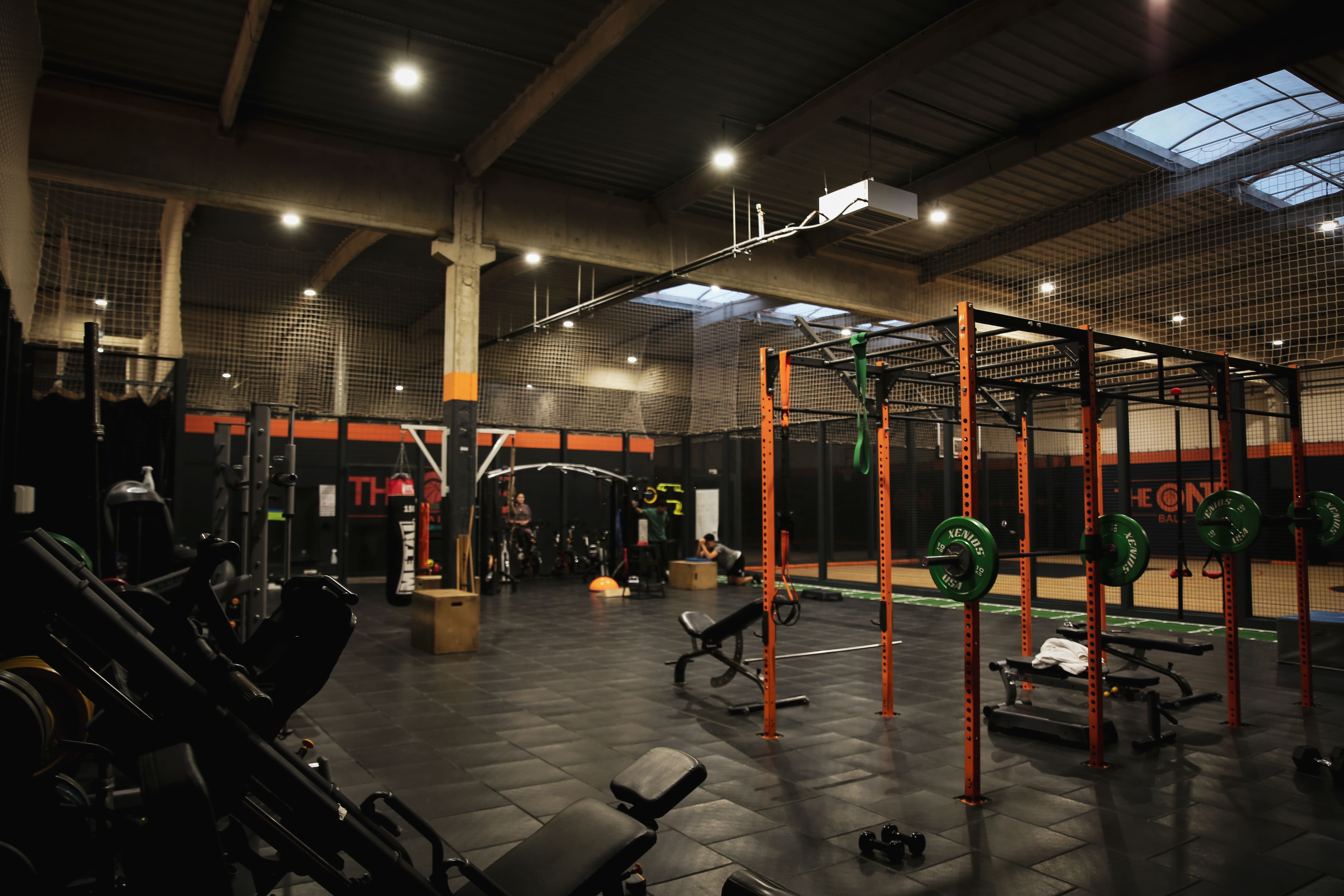 Intérieur d'une salle de sport équipée pour CrossFit avec cages de musculation orange, poids verts et bancs de musculation.