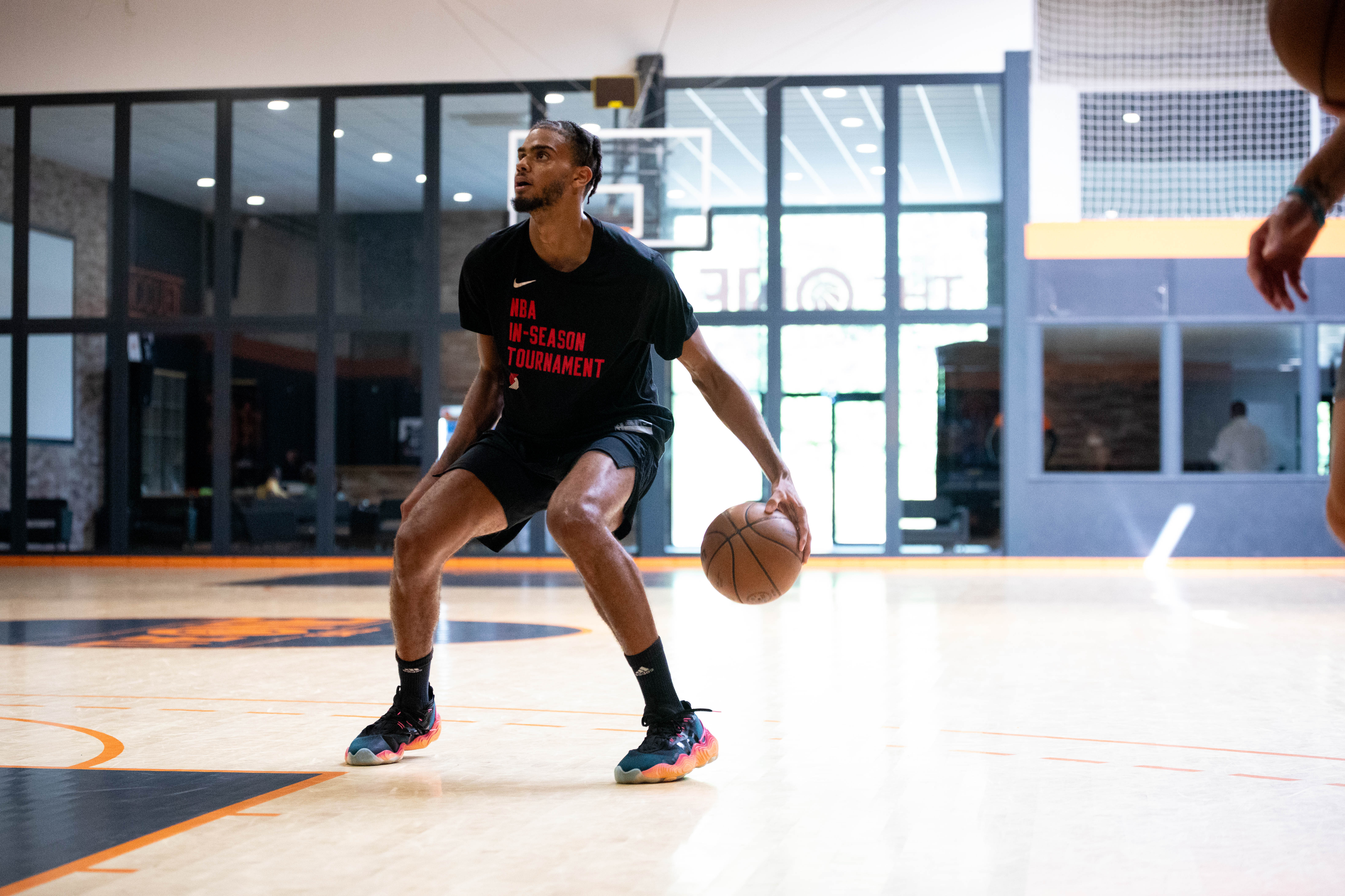 Un joueur de basketball dribble sur un terrain intérieur, portant un t-shirt noir avec l'inscription NBA In-Season Tournament.