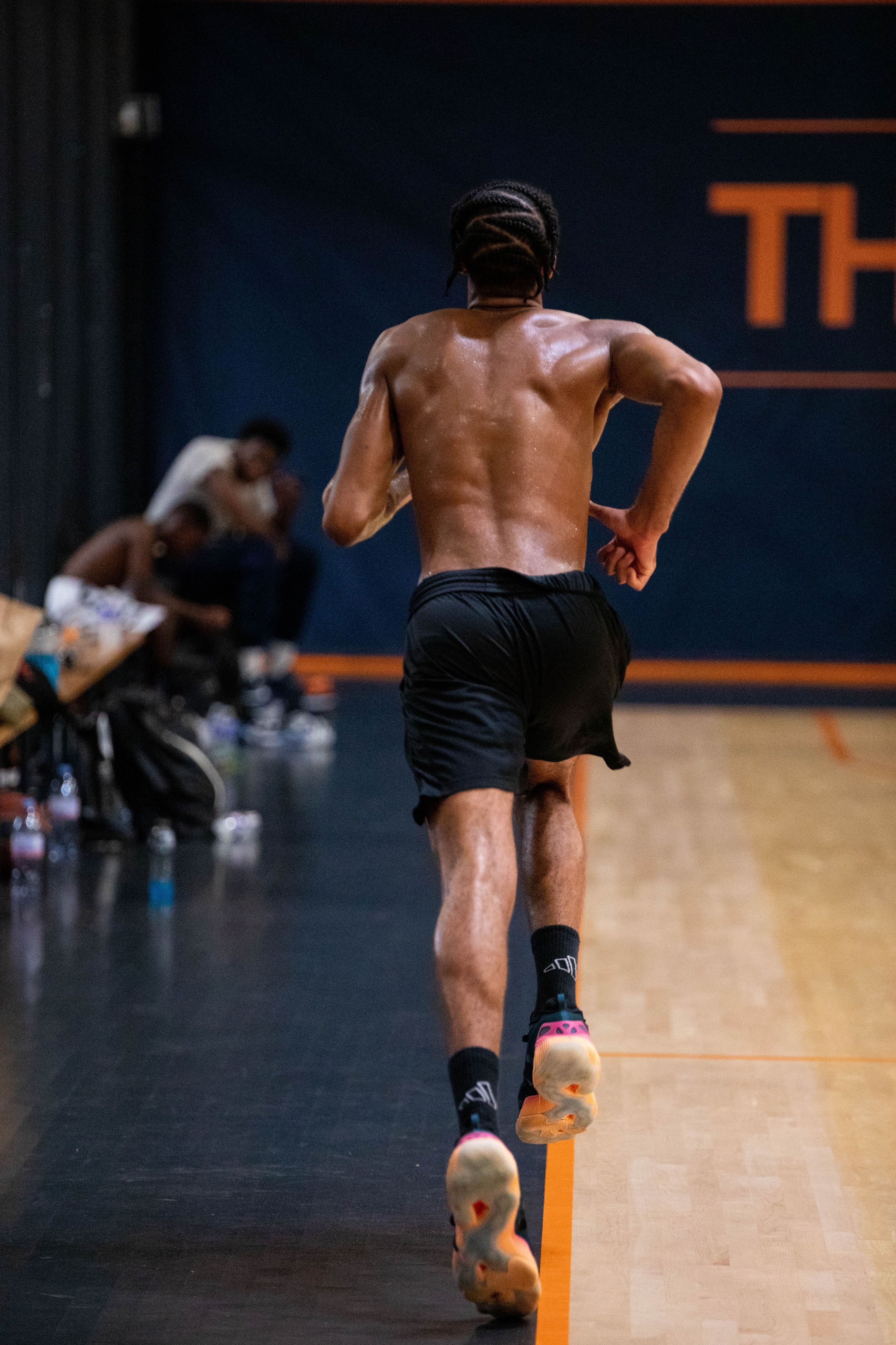 Homme torse nu en short noir courant sur un terrain de basketball intérieur.