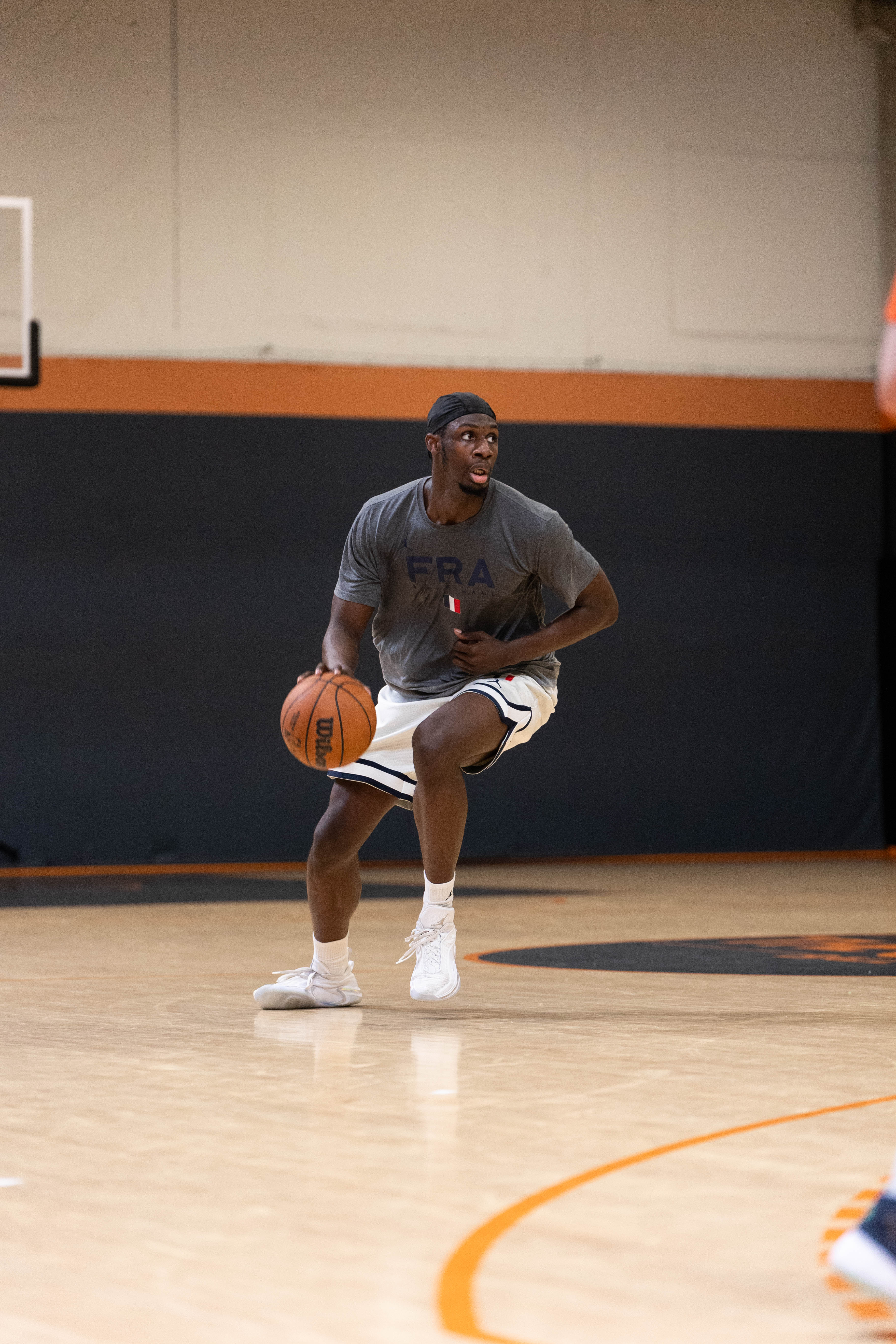 Joueur de basket masculin dribblant un ballon sur un terrain de basketball intérieur.
