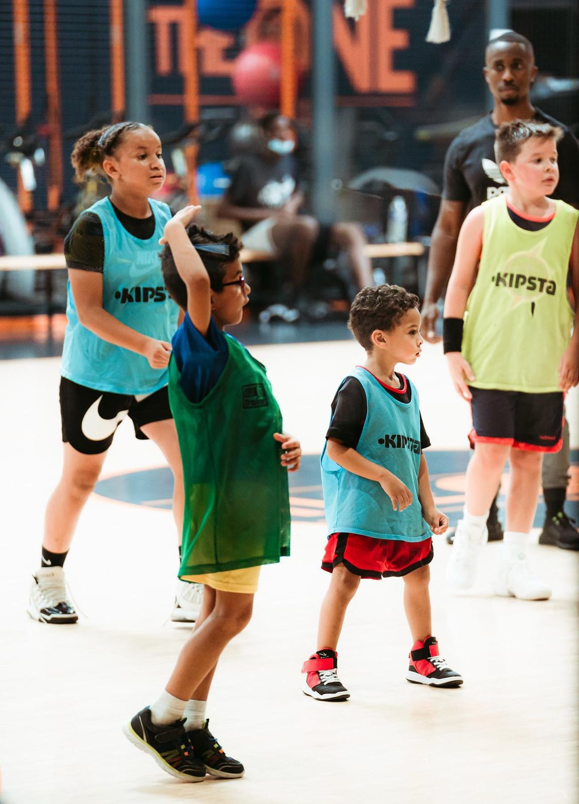 Des enfants jouent au basket à l'intérieur sous la supervision d'un entraîneur.