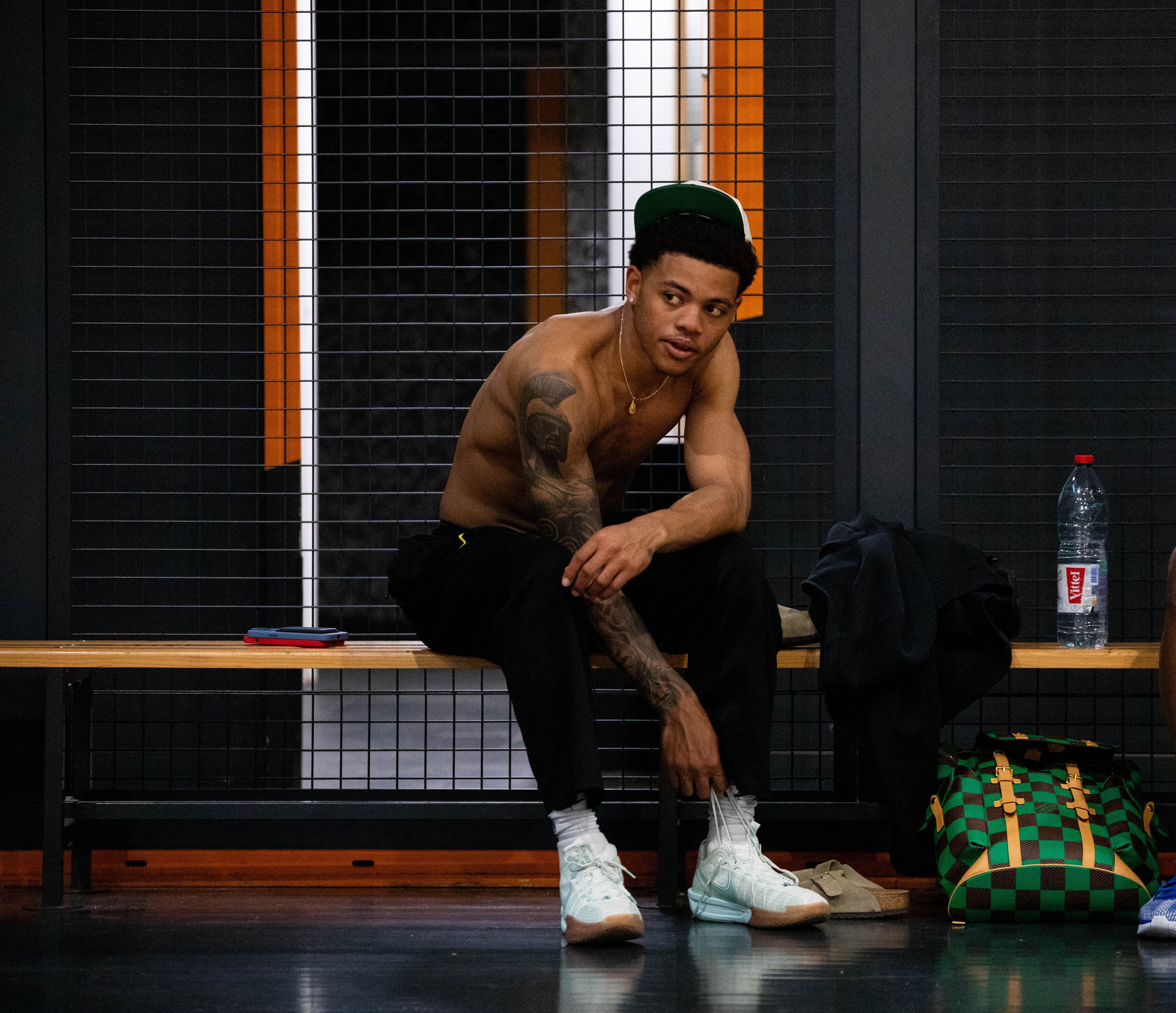 Homme tatoué portant un débardeur noir avec logo 'Puma Hoops' dans une salle de sport.