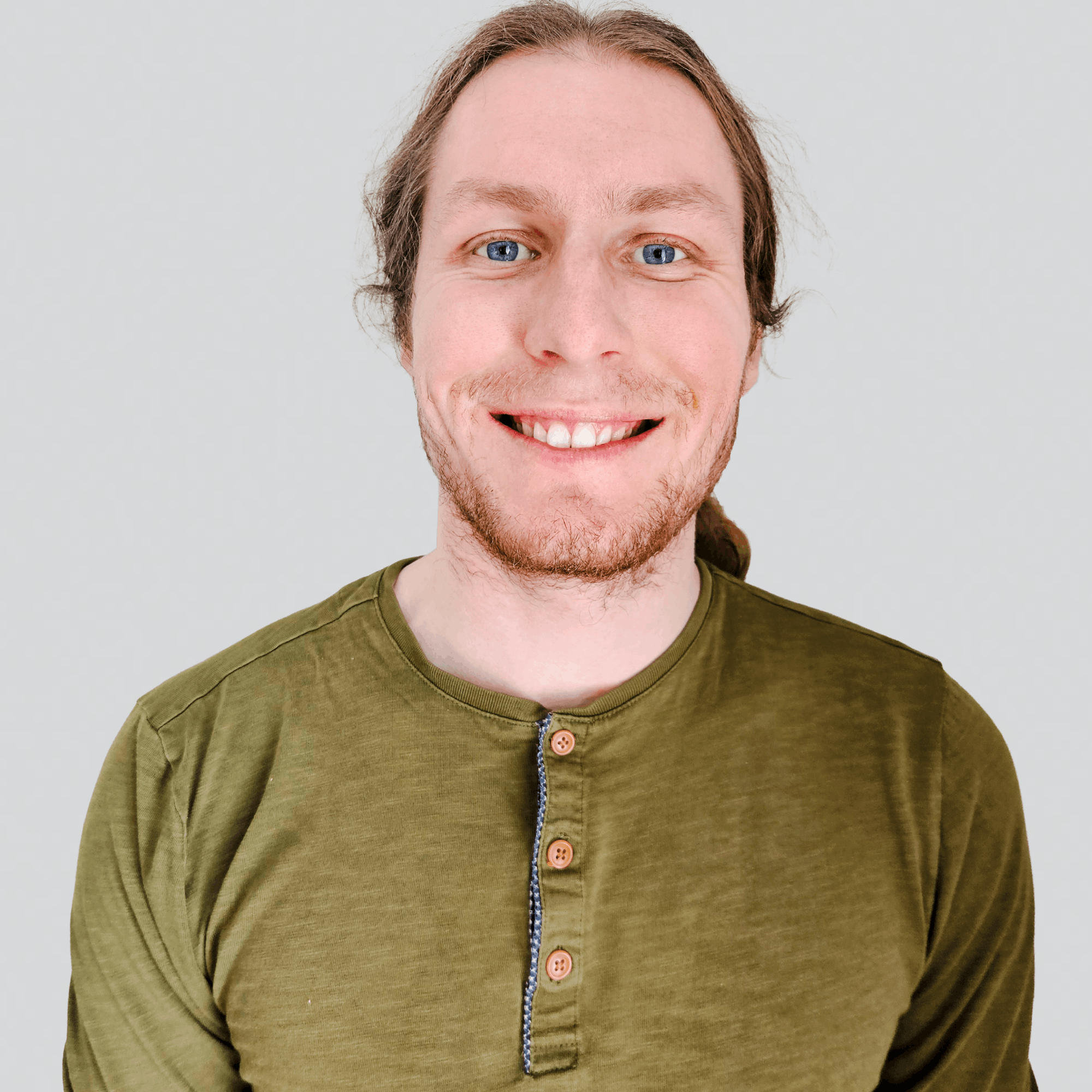 Smiling man with blue eyes and light brown hair wearing an olive green Henley shirt against a plain light gray background.