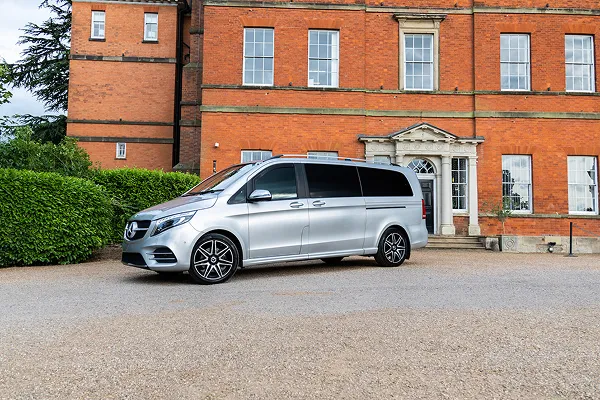 Silver Mercedes-Benz van parked in front of a large brick building with white framed windows and an ornate entrance.