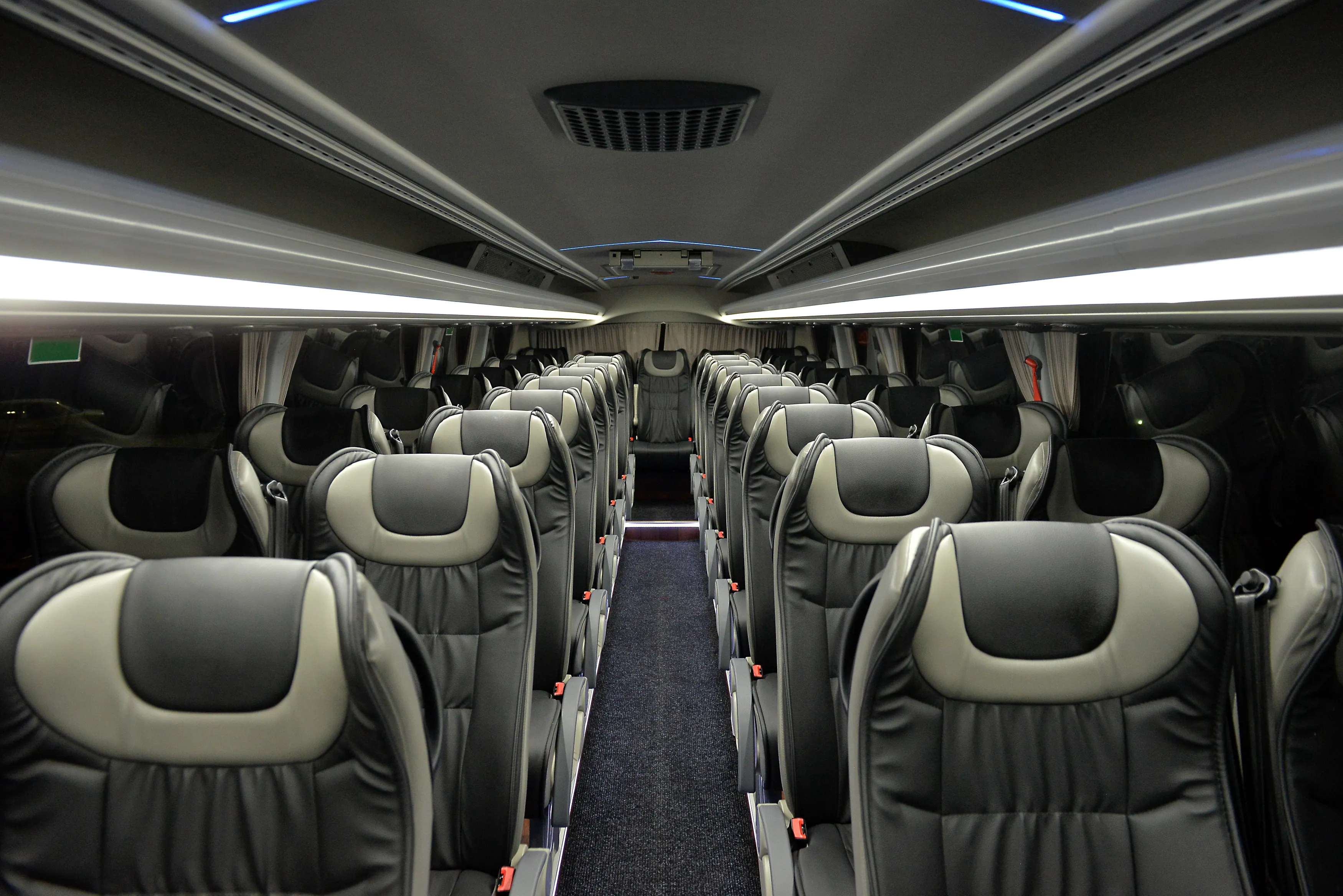 Interior view of an empty modern passenger bus with black and gray leather seats arranged in rows along a central aisle.