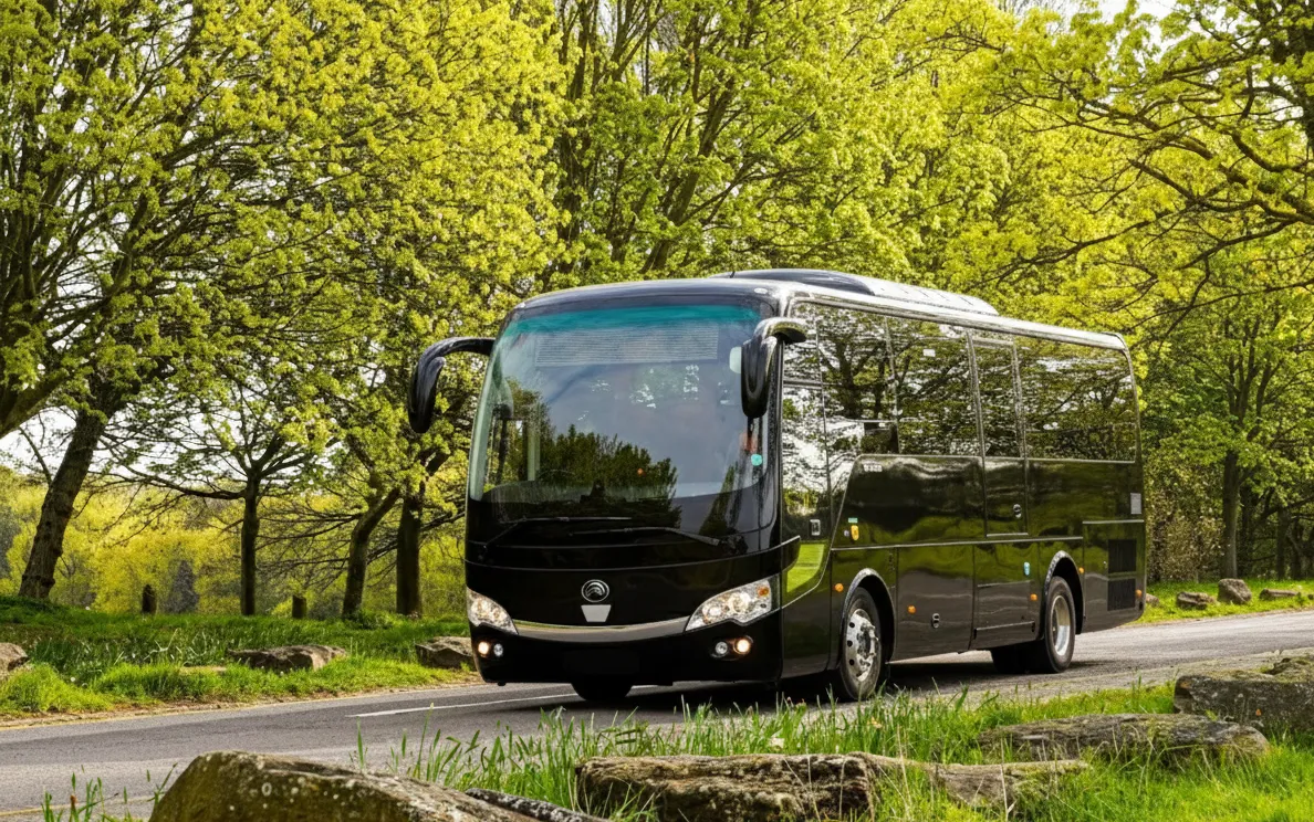 Black coach bus driving on a road lined with green trees and rocks.