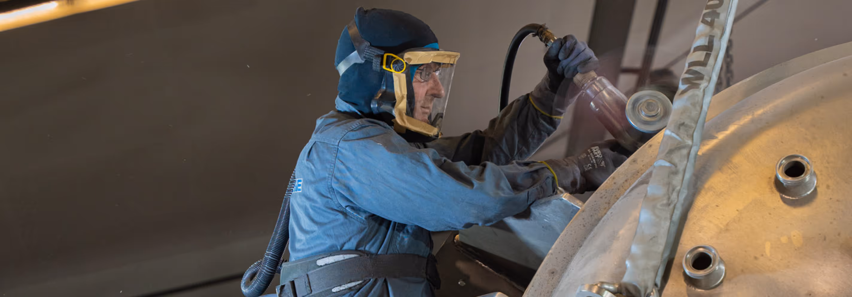 Arbeiter in Schutzkleidung und Atemschutzgerät schleift Metalloberfläche mit Winkelschleifer.