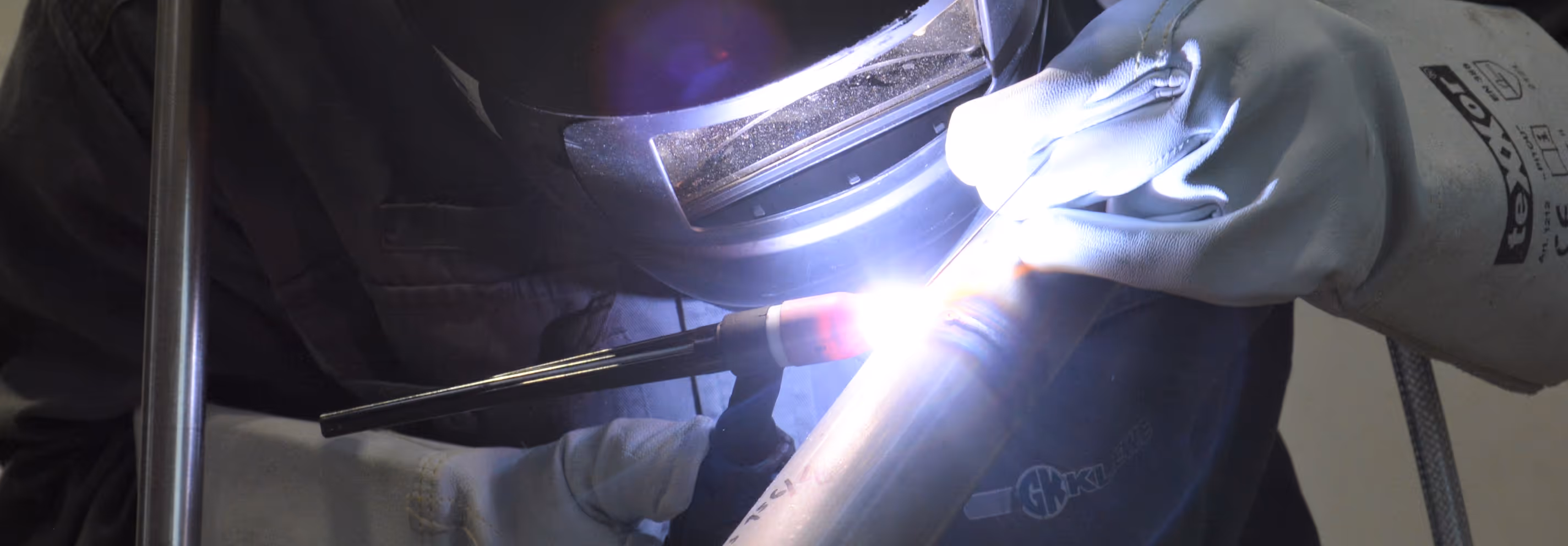 Schweißer in Schutzkleidung schweißt ein Metallrohr mit Lichtbogen.