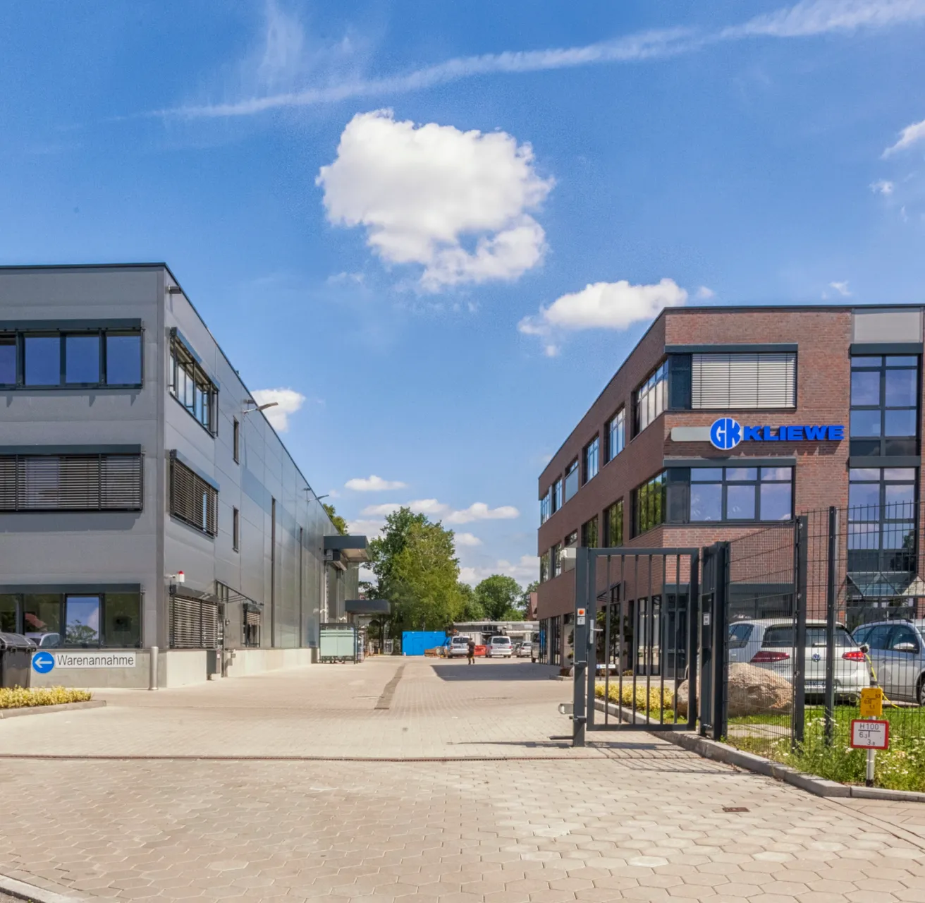 Firmengebäude von GK Kliewe neben einem Parkplatz mit Autos und einem blauen Himmel mit Wolken.