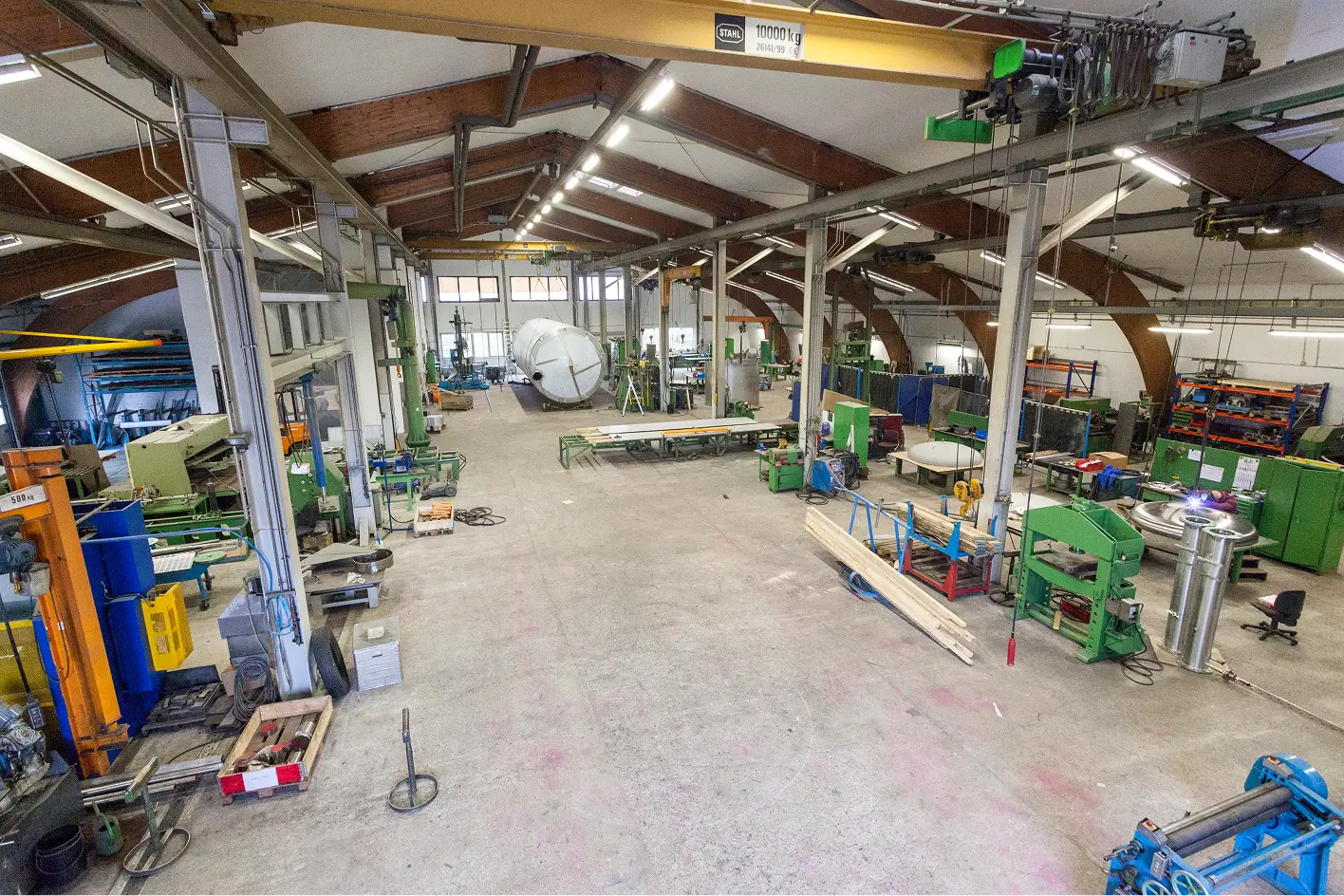 Große Produktionshalle mit verschiedenen Maschinen, Werkbänken und einem großen zylindrischen Metallbehälter im Hintergrund.