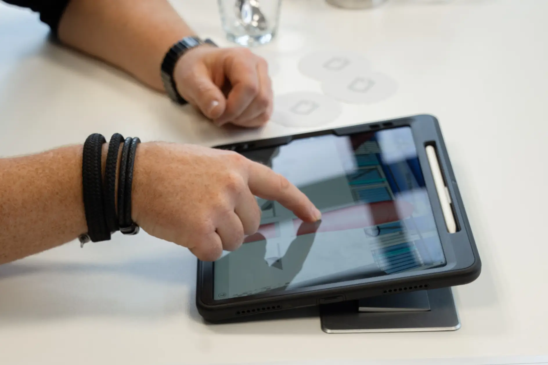 Hand berührt den Bildschirm eines Tablets auf einem weißen Tisch, eine andere Hand ruht daneben.