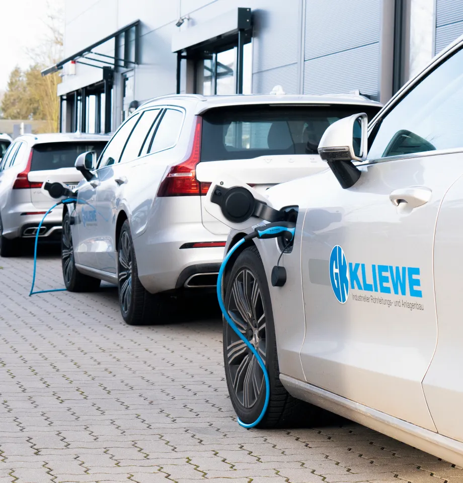 Weiße Elektroautos, die an einer Ladestation neben einem modernen Gebäude auf einem Parkplatz aufgeladen werden.