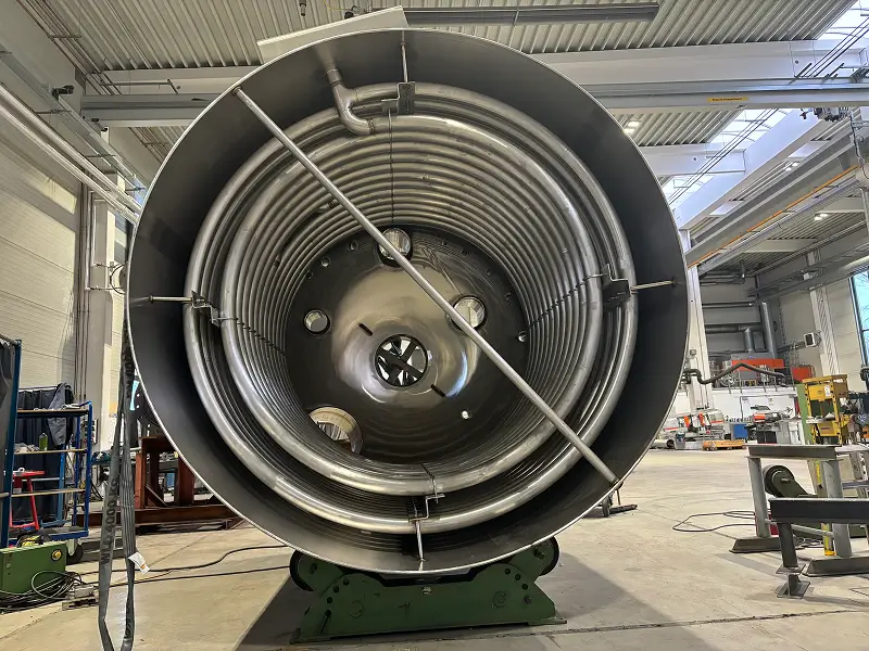 Großes Metallrohr mit spiralförmig angeordneten Rohren im Inneren in einer Industriehalle.