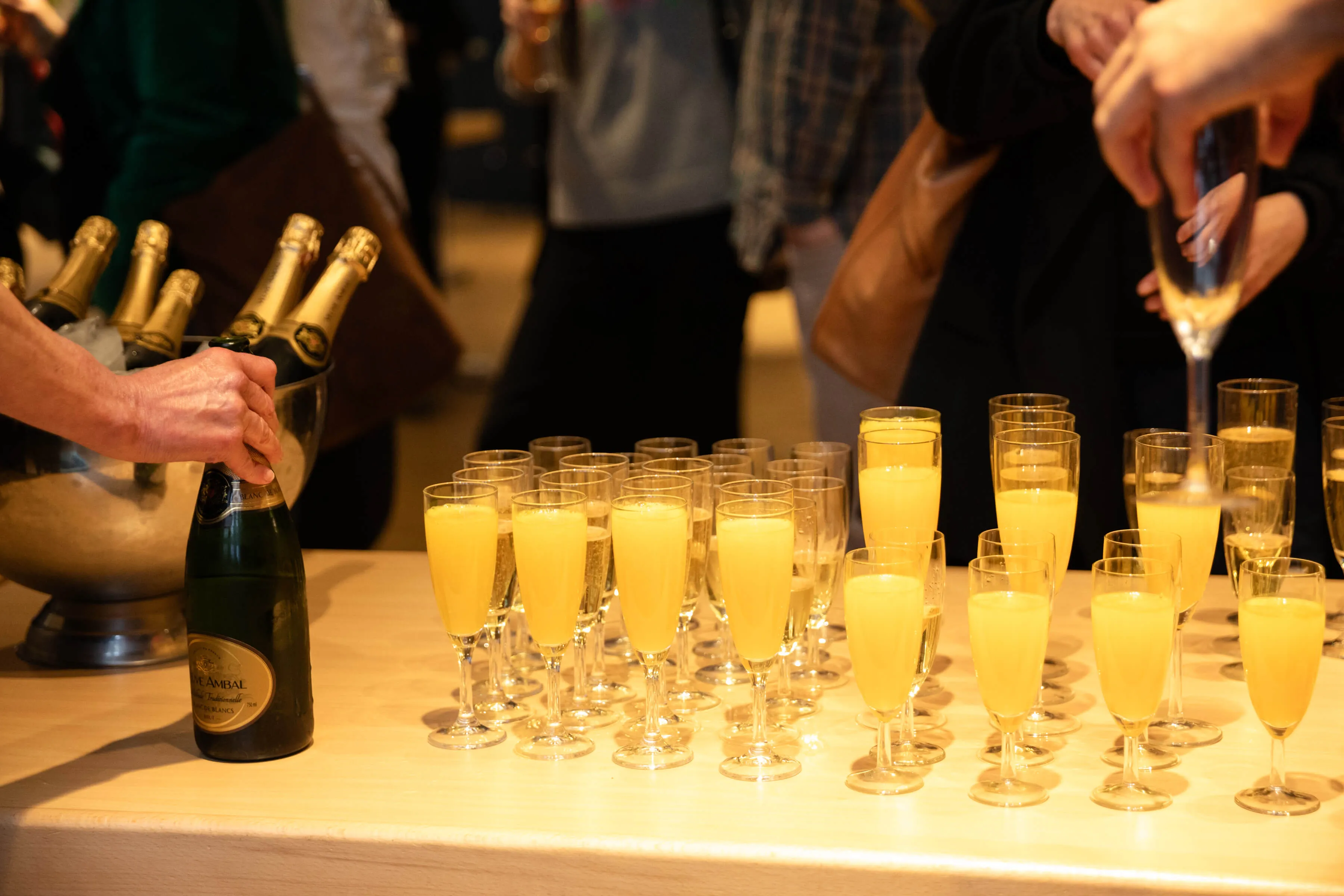 Mit Sekt bzw. Orangesaft gefüllte Sektgläser auf einem Tisch, einzelne Hände greifen danach.