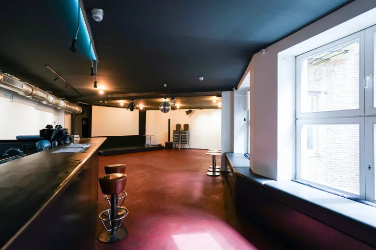 Blick vom Eingang auf die Bühne des Veranstaltungsraums, links sieht man die Bartheke