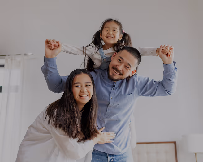 Smiling family with father carrying young daughter on shoulders and mother leaning close.