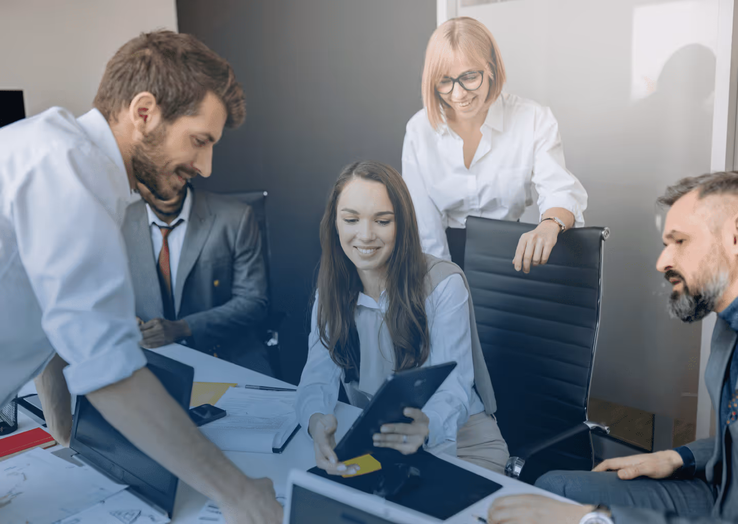 A group of five business professionals collaborating around a table with laptops and documents in an office.