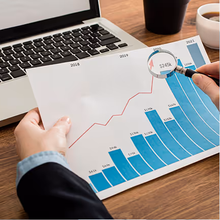 Person holding a chart with year-by-year bar and line graphs displaying financial growth from 2018 to 2021, with a magnifying glass highlighting $245k in 2020.