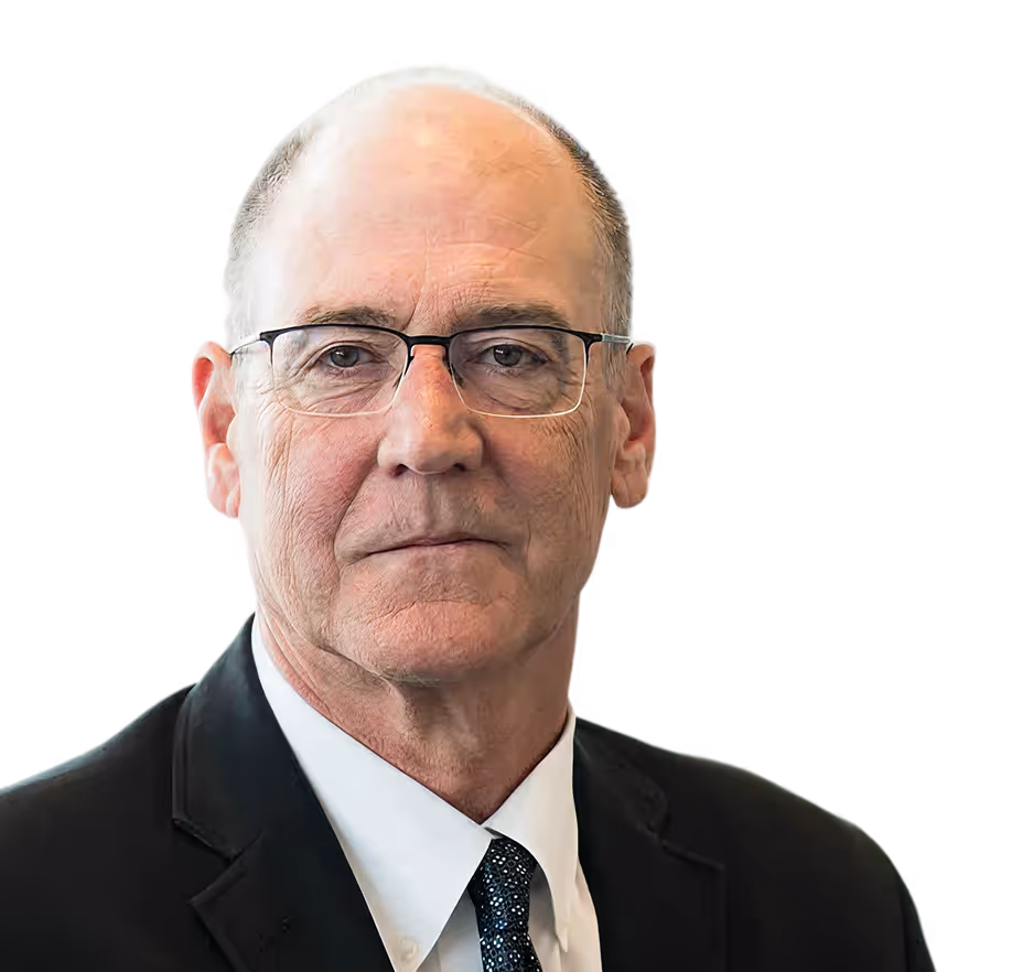 Portrait of an older man with glasses wearing a black suit, white shirt, and patterned tie against a black background.