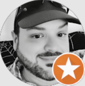Close-up black and white photo of a man with a beard and a cap smiling, with an orange and white star icon overlay.