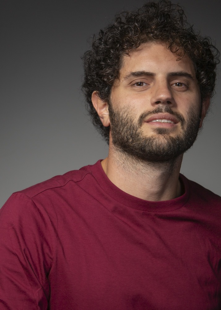 Porträtfoto von Costantino Buttitta, ein junger Mann mit lockigen braunen Haaren und Bart in einem dunkelroten T-Shirt