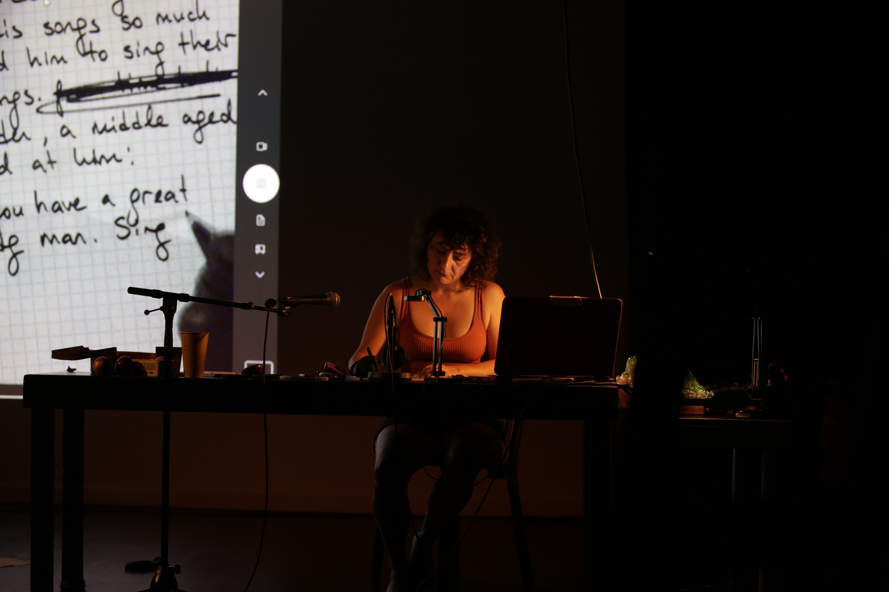 İpek Seyalıoğlu sitzt auf einer Bühne an einem Schreibtisch und schreibt etwas mit einem Stift auf Papier