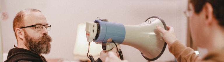 Ein Mann mit Vollbart und Brille hält ein Megaphon