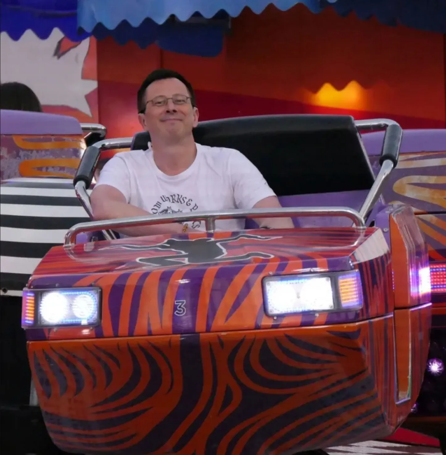 Mathias Traxler sitzt in einem Jahrmarkt Fahrgeschäft, trägt ein weißes Tshirt und lächelt in die Kamera.