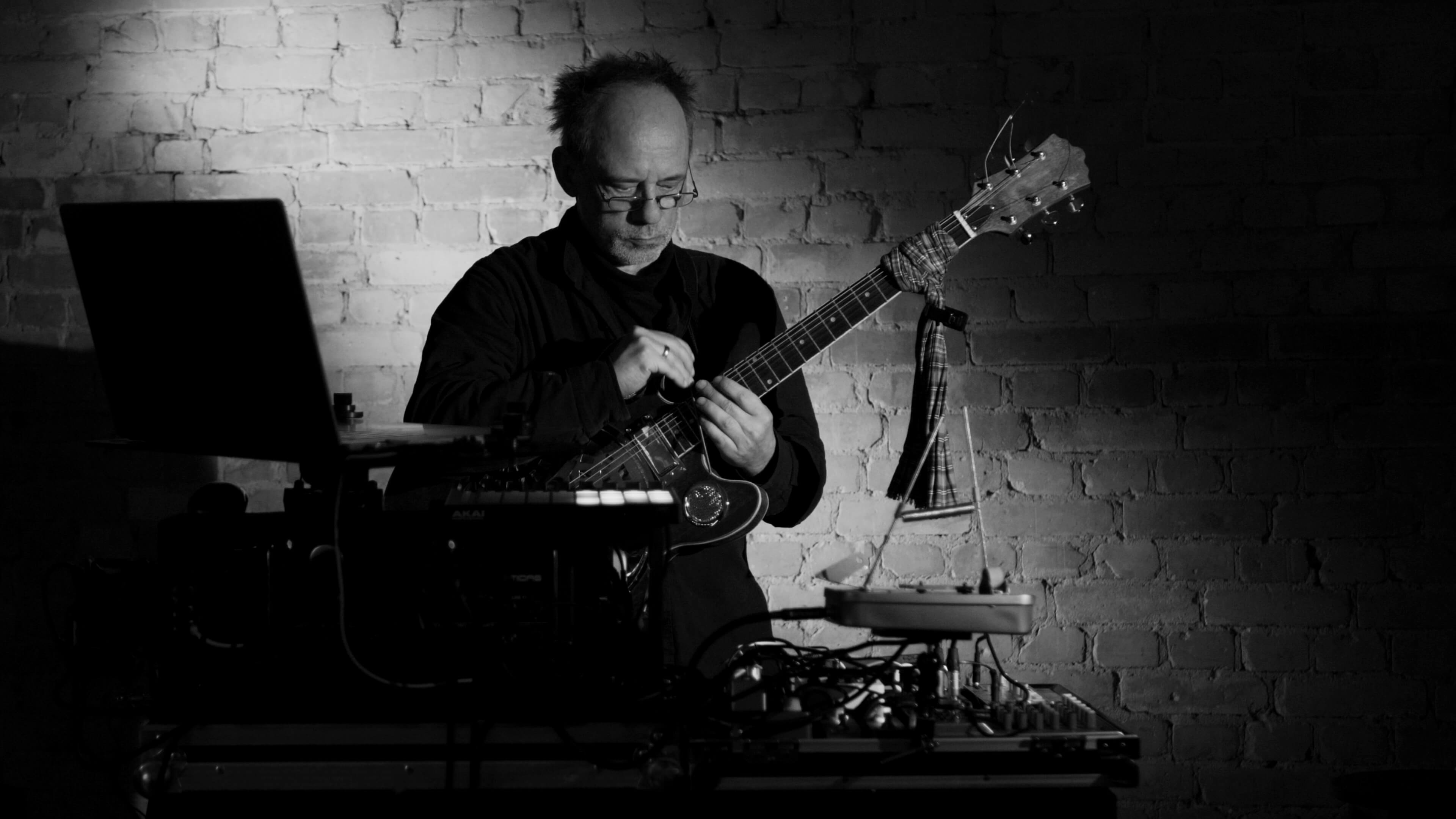 Frank steht an einem Mischpult und spielt Gitarre