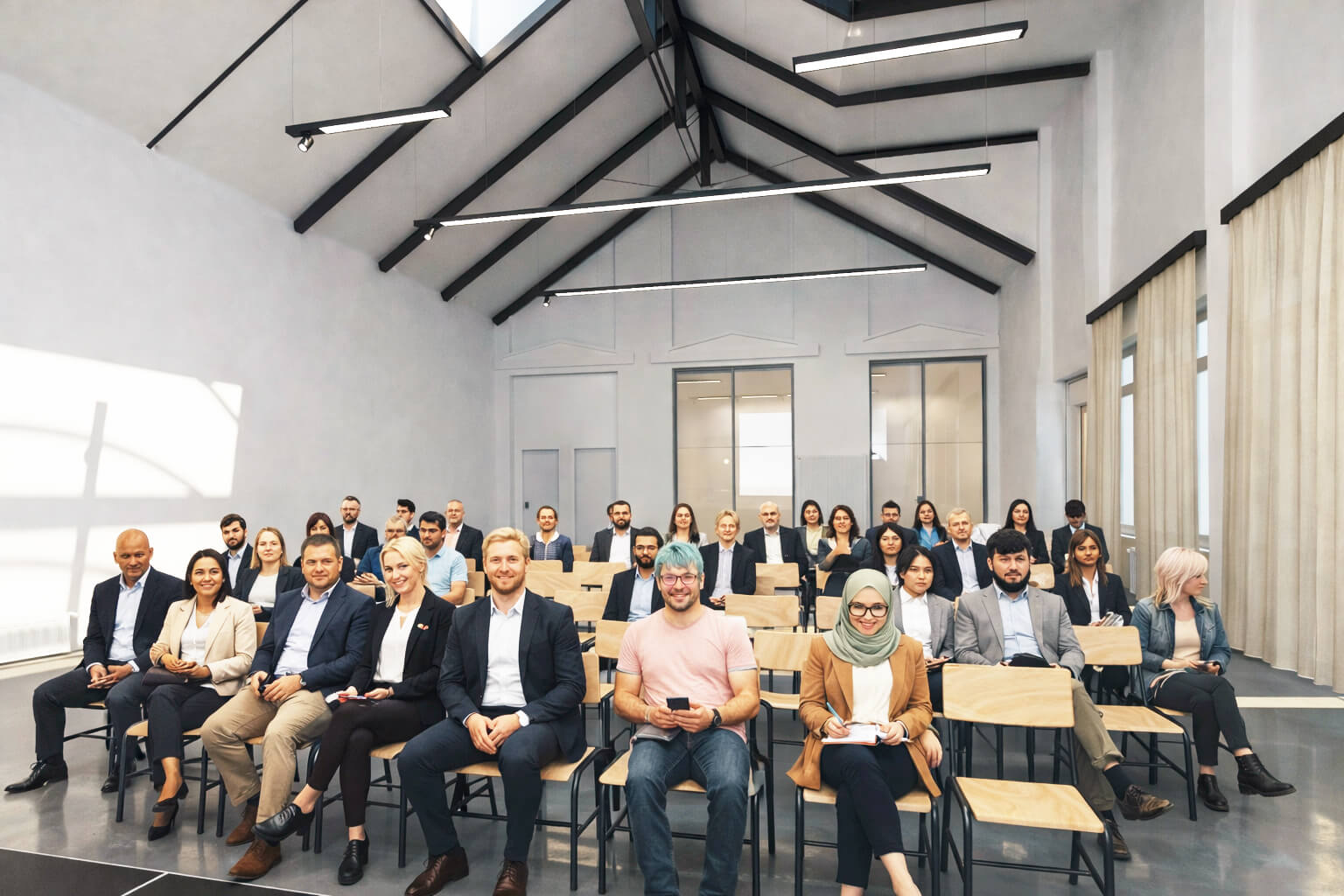 Veranstaltungssaal mit vielen Stuhlreihen, auf denen Menschen sitzen