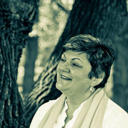 Ein grünlich schwarzweißes Porträtfoto von Slavica Klimkowsky. Sie schaut an der Kamera vorbei, lächelt und steht vor einem Baum.