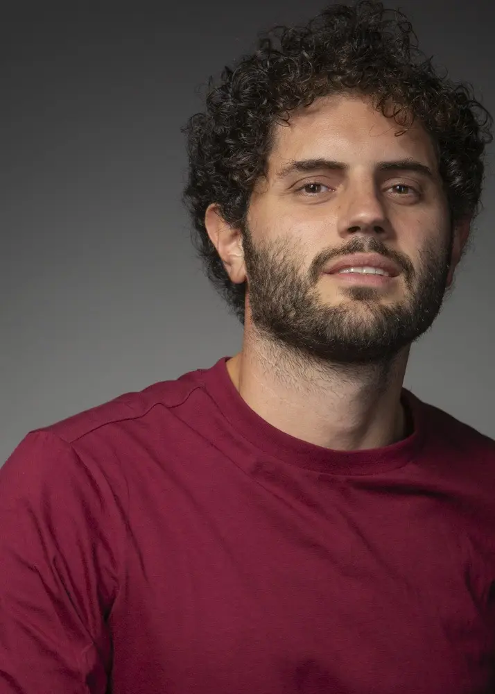Porträtfoto von Costantino Buttitta, ein junger Mann mit lockigen braunen Haaren und Bart in einem dunkelroten T-Shirt