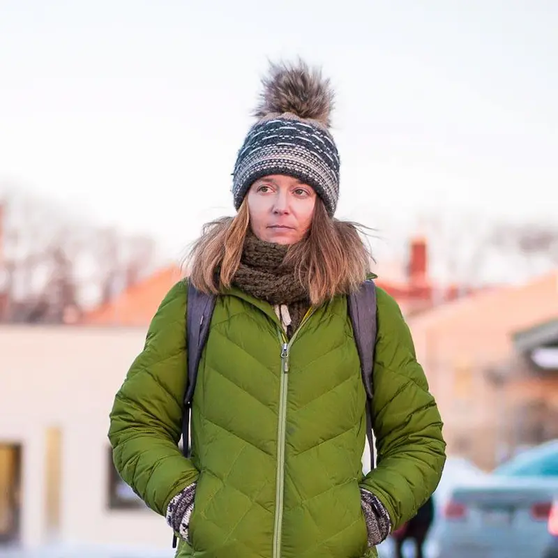 Frau in grüner Winterjacke, mit braunem Schal und graublau gemusterter Bommelmütze
